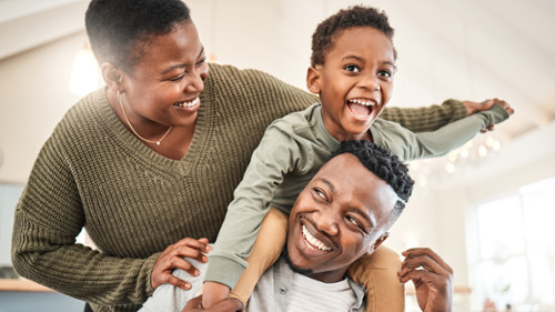 Happy family of three laughing together at home, showcasing confident bright smiles