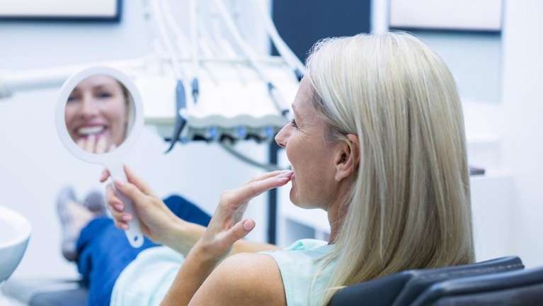 Woman in dental chair holding mirror looking at her dental implants, winston-salem nc