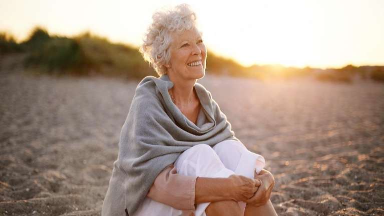 Older woman sitting on the beach smiling after getting dentures, winston salem nc